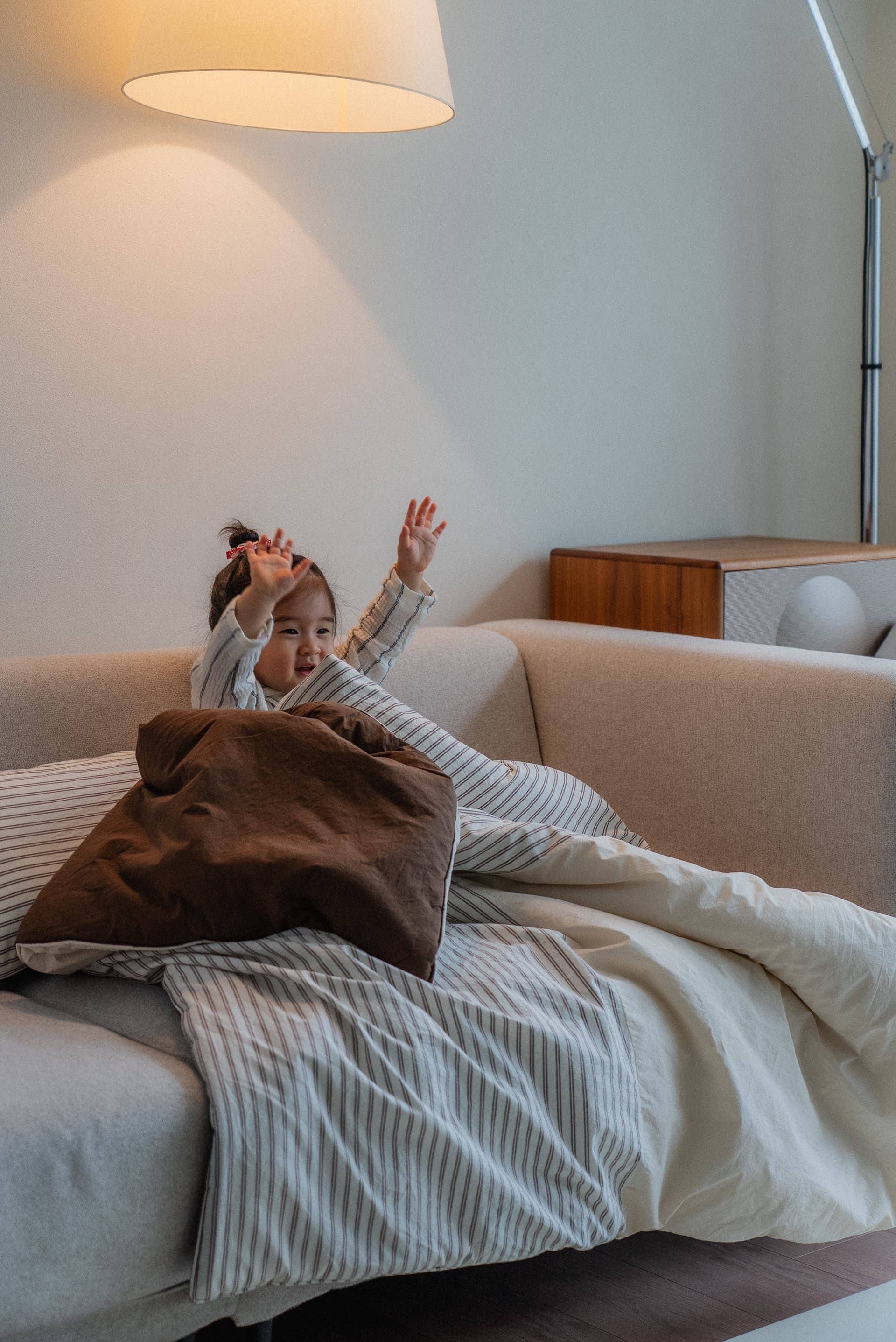 A cozy child sitting on a sofa wrapped in soft bedding.